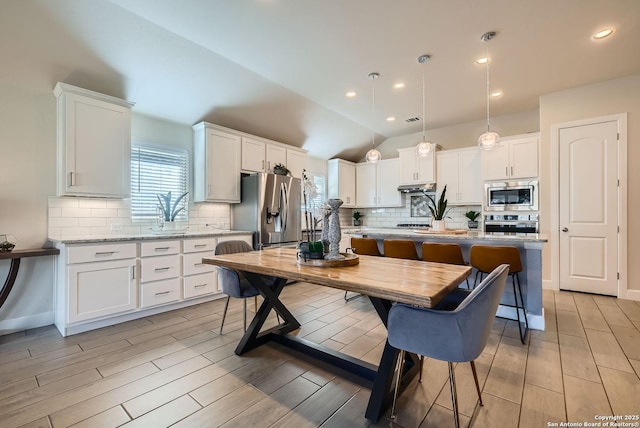 kitchen with hanging light fixtures, a center island with sink, stainless steel appliances, light stone countertops, and white cabinets