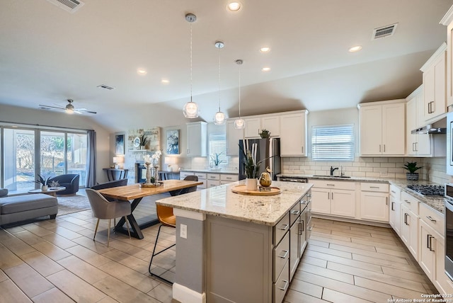 kitchen with decorative light fixtures, white cabinets, decorative backsplash, a center island, and stainless steel appliances