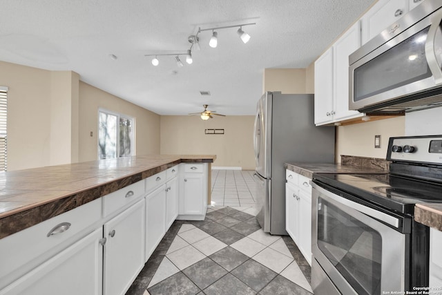 kitchen featuring ceiling fan, appliances with stainless steel finishes, white cabinetry, a textured ceiling, and wood counters