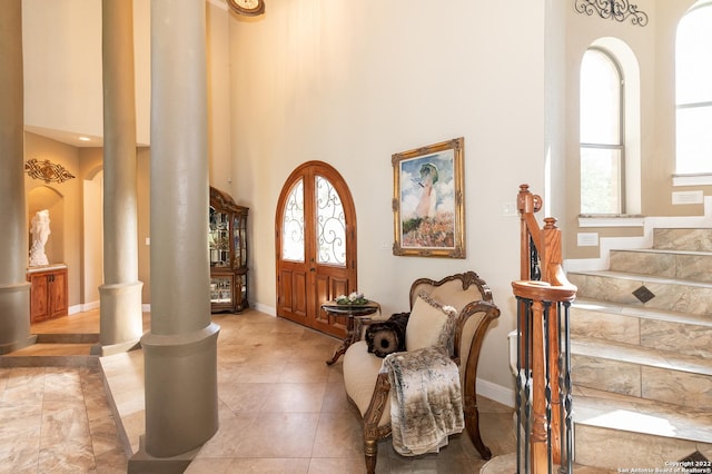 foyer with a towering ceiling, decorative columns, and light tile patterned floors