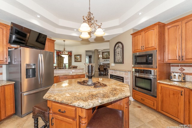 kitchen featuring appliances with stainless steel finishes, decorative light fixtures, a center island, and a raised ceiling