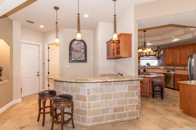 bar with light stone counters, appliances with stainless steel finishes, and hanging light fixtures