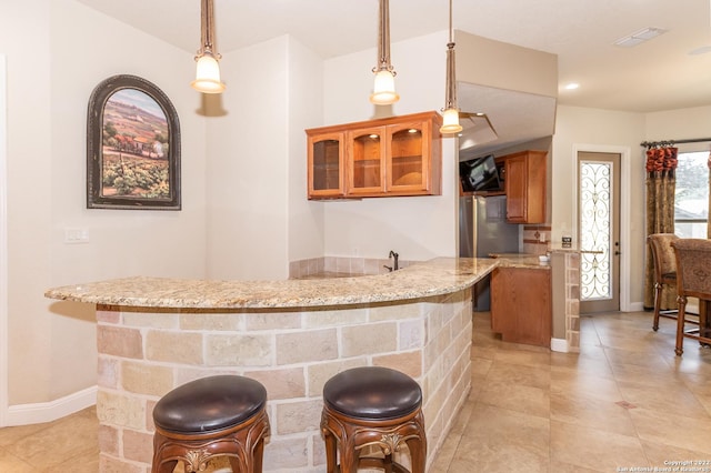 kitchen featuring light stone counters, light tile patterned floors, a kitchen breakfast bar, kitchen peninsula, and pendant lighting