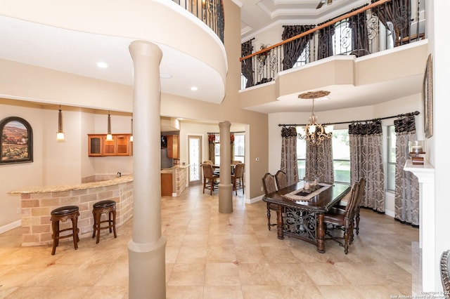 dining area featuring bar, ornate columns, crown molding, a chandelier, and a high ceiling