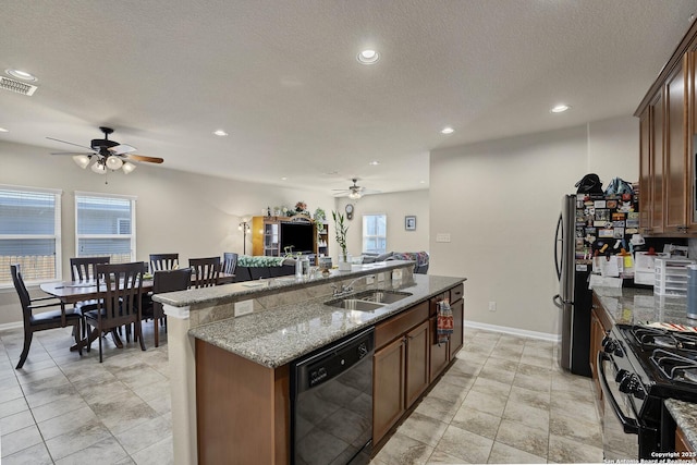 kitchen with gas stove, light stone counters, a textured ceiling, black dishwasher, and a kitchen island with sink