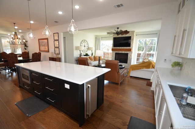 kitchen featuring hanging light fixtures, a kitchen island, a large fireplace, and white cabinets