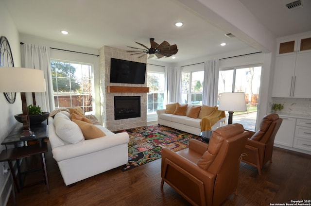 living room featuring a tile fireplace, a healthy amount of sunlight, dark wood-type flooring, and ceiling fan