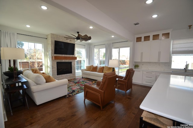 living room with dark wood-type flooring, sink, a large fireplace, beamed ceiling, and ceiling fan