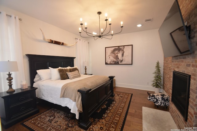 bedroom with a brick fireplace, dark wood-type flooring, and an inviting chandelier