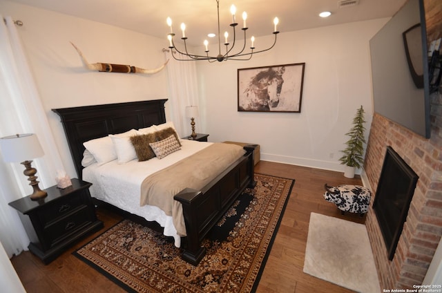 bedroom with a brick fireplace and dark wood-type flooring