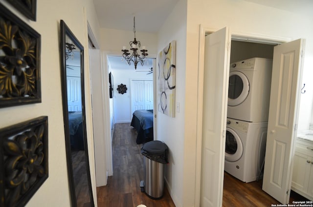 clothes washing area featuring stacked washer / dryer, dark hardwood / wood-style flooring, and a notable chandelier