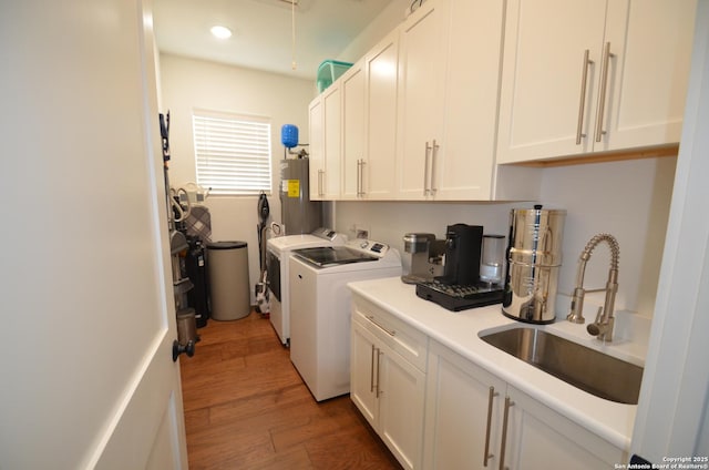 washroom featuring sink, water heater, washing machine and dryer, dark hardwood / wood-style floors, and cabinets