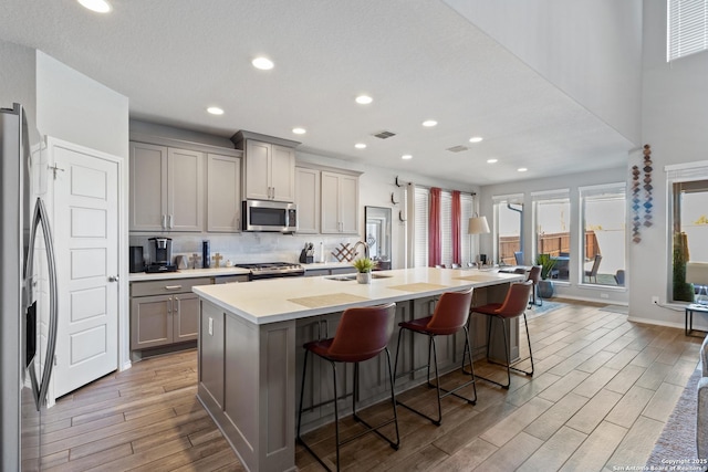 kitchen featuring a kitchen bar, sink, gray cabinetry, appliances with stainless steel finishes, and an island with sink