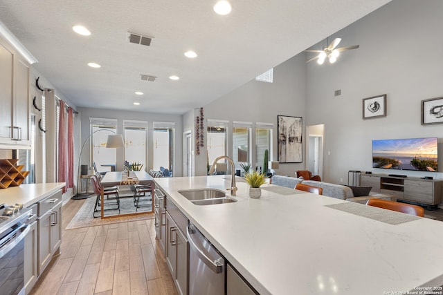 kitchen with sink, light wood-type flooring, a kitchen island with sink, stainless steel appliances, and a textured ceiling