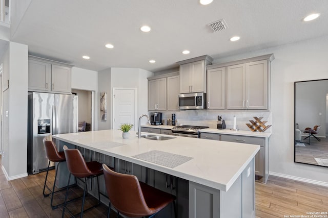 kitchen featuring stainless steel appliances, a center island with sink, sink, and gray cabinetry