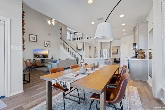 dining area featuring a high ceiling, ceiling fan, and light hardwood / wood-style flooring