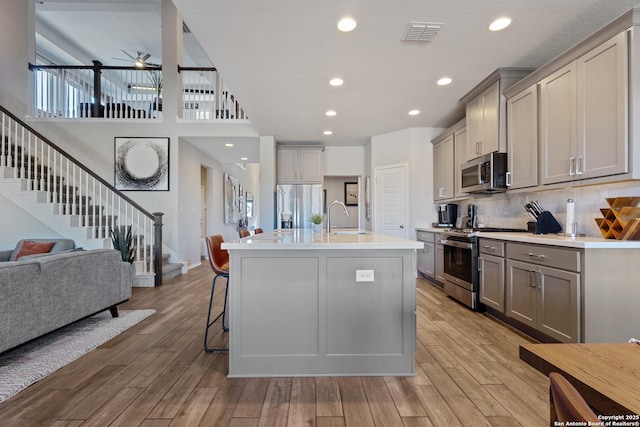 kitchen featuring a breakfast bar, sink, gray cabinetry, an island with sink, and stainless steel appliances