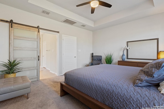 bedroom featuring ceiling fan, a tray ceiling, a barn door, and light carpet