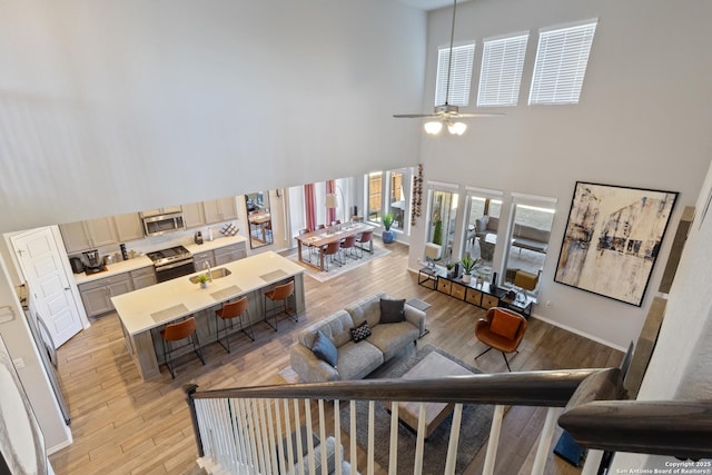 living room featuring a towering ceiling, ceiling fan, and light hardwood / wood-style flooring