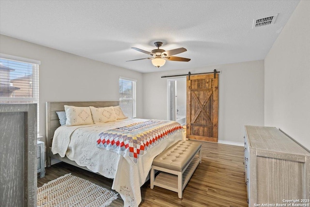 bedroom with ceiling fan, dark hardwood / wood-style floors, a barn door, and a textured ceiling