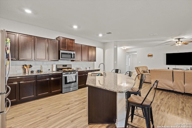 kitchen featuring sink, light stone counters, light wood-type flooring, stainless steel appliances, and a kitchen island with sink