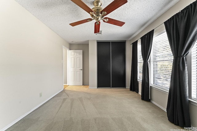 unfurnished bedroom featuring ceiling fan, light colored carpet, and a textured ceiling