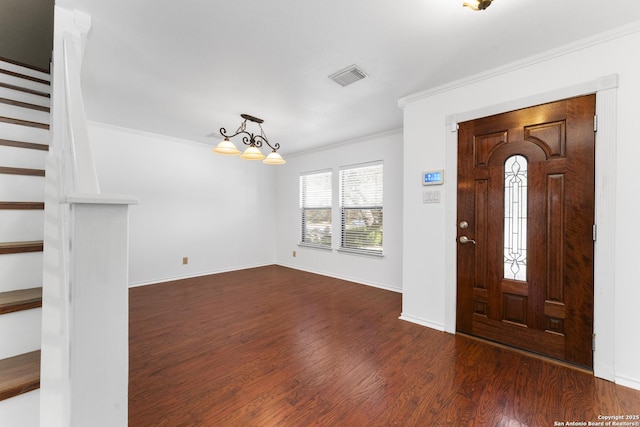 foyer entrance with an inviting chandelier, dark wood-type flooring, and ornamental molding