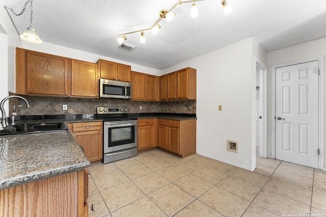 kitchen featuring sink, hanging light fixtures, light tile patterned floors, appliances with stainless steel finishes, and backsplash