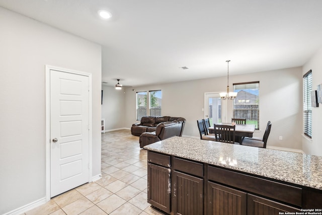 kitchen with light tile patterned floors, hanging light fixtures, light stone counters, dark brown cabinetry, and a chandelier