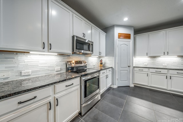 kitchen with stainless steel appliances, white cabinetry, and dark stone countertops