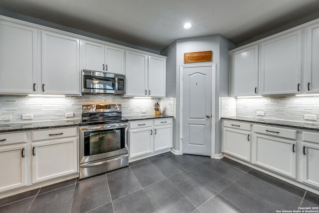 kitchen with white cabinetry, appliances with stainless steel finishes, dark tile patterned floors, and dark stone countertops