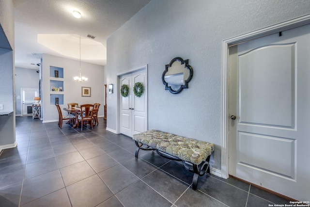 foyer entrance featuring a chandelier, dark tile patterned flooring, and a textured ceiling