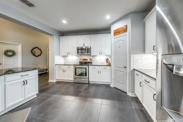 kitchen featuring stainless steel appliances, white cabinetry, dark stone countertops, and decorative backsplash