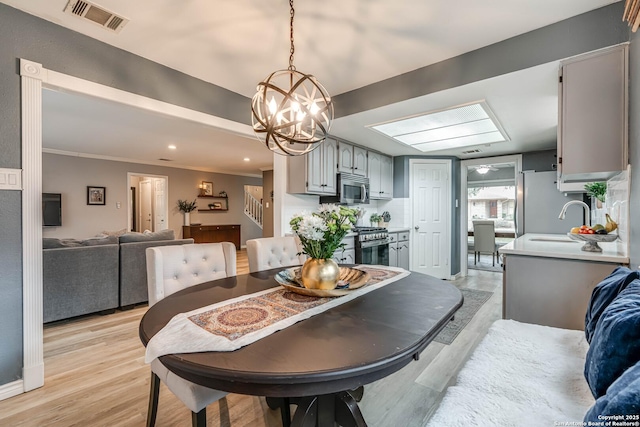 dining room with sink, light hardwood / wood-style flooring, ornamental molding, and a chandelier