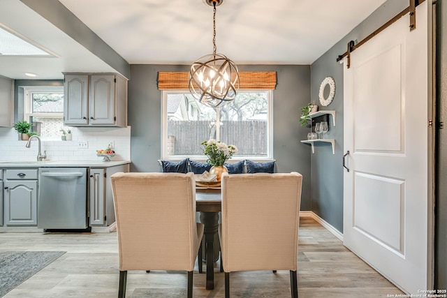 dining room with a barn door, sink, a notable chandelier, and light hardwood / wood-style flooring