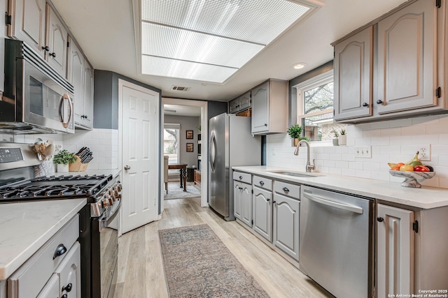 kitchen with appliances with stainless steel finishes, sink, light hardwood / wood-style floors, and plenty of natural light