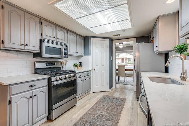 kitchen with appliances with stainless steel finishes, sink, light hardwood / wood-style floors, and decorative backsplash