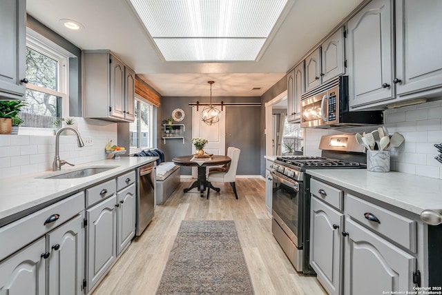 kitchen with sink, hanging light fixtures, light hardwood / wood-style flooring, gray cabinets, and stainless steel appliances