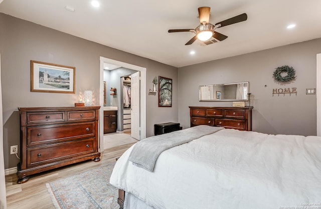 bedroom with ensuite bath, a spacious closet, ceiling fan, and light hardwood / wood-style flooring