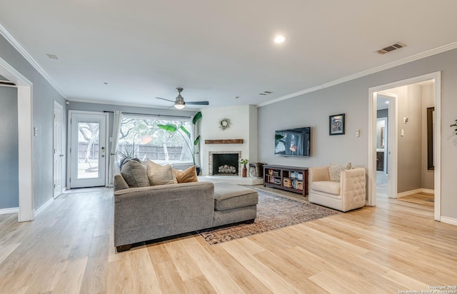 living room with crown molding, ceiling fan, a fireplace, and light wood-type flooring