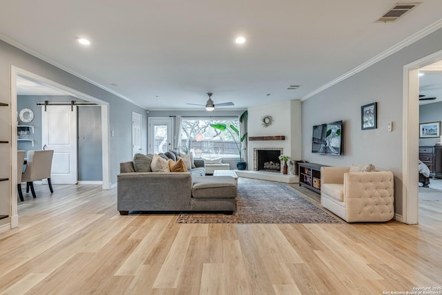 living room featuring crown molding, a barn door, ceiling fan, and light hardwood / wood-style flooring