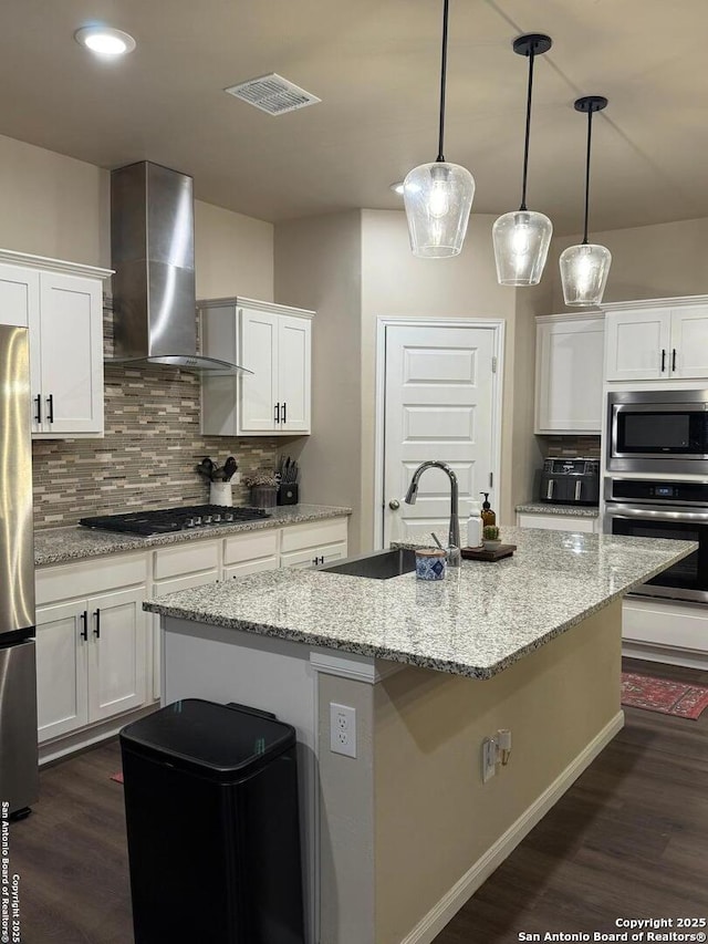 kitchen featuring wall chimney exhaust hood, sink, white cabinetry, decorative light fixtures, and appliances with stainless steel finishes