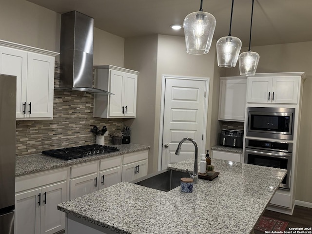 kitchen with appliances with stainless steel finishes, white cabinetry, sink, a center island with sink, and wall chimney exhaust hood