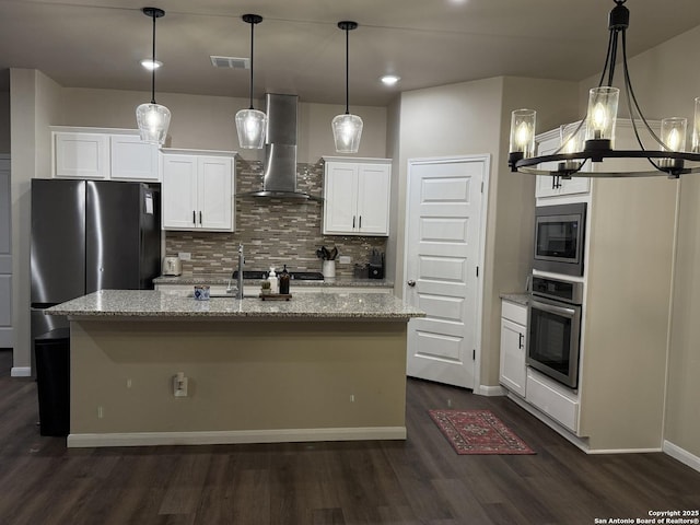 kitchen featuring wall chimney range hood, white cabinetry, a kitchen island with sink, stainless steel appliances, and light stone counters