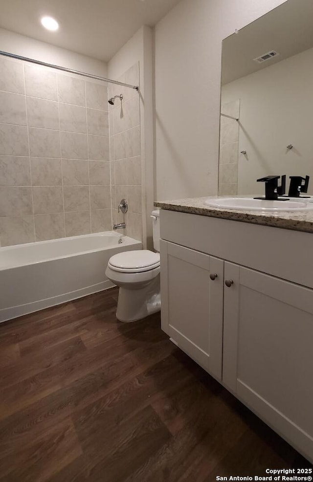 full bathroom with hardwood / wood-style flooring, vanity, tiled shower / bath, and toilet