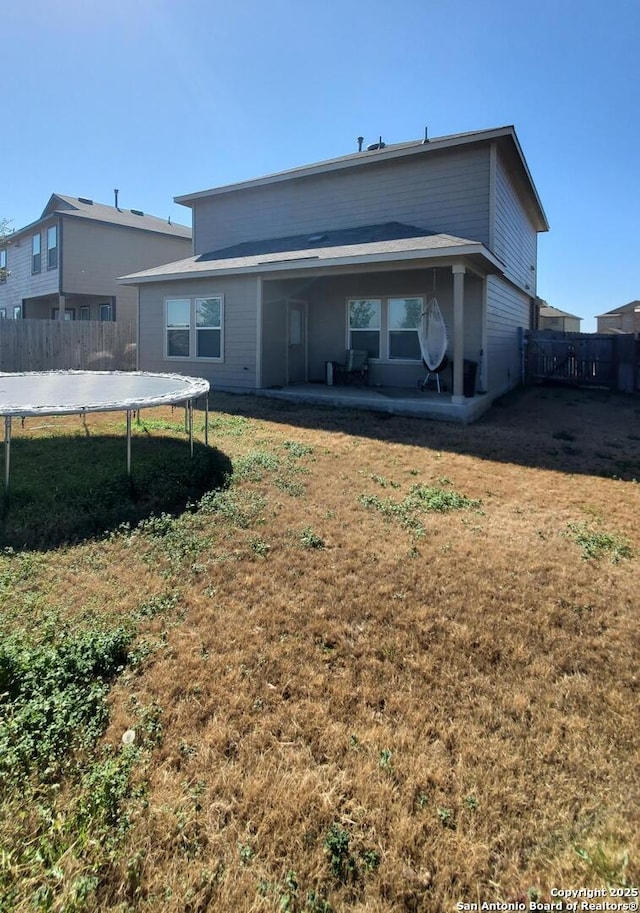 back of house featuring a patio, a trampoline, and a lawn