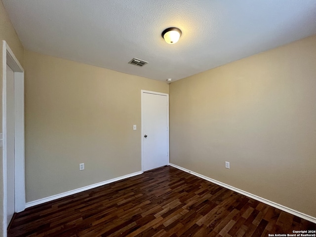 spare room featuring a textured ceiling and dark hardwood / wood-style flooring