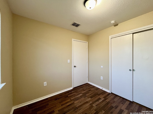 unfurnished bedroom featuring a closet, dark hardwood / wood-style floors, and a textured ceiling