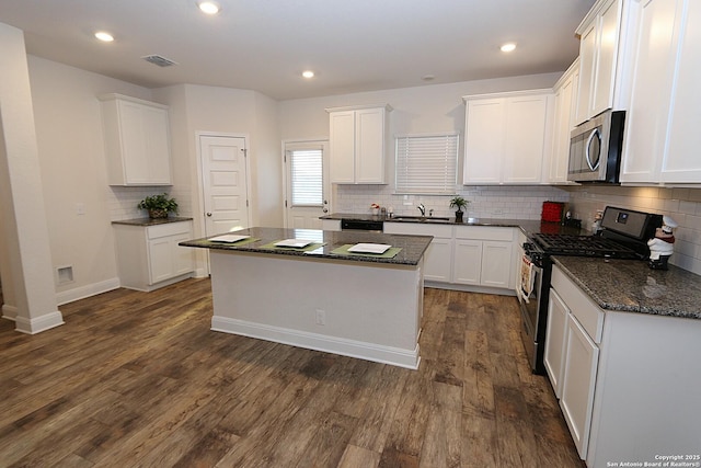 kitchen with white cabinetry, appliances with stainless steel finishes, dark hardwood / wood-style flooring, a kitchen island, and dark stone counters