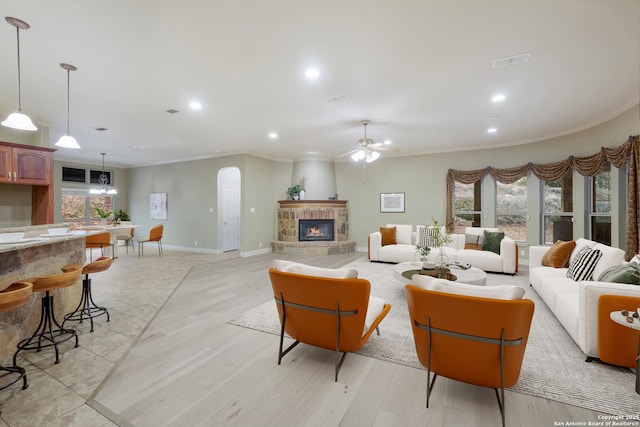 living room with a fireplace, ornamental molding, ceiling fan, and light wood-type flooring